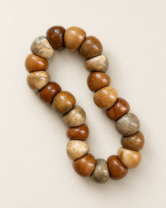 Kuke bracelet with irregular swirl-pattern beads on a warm ivory surface